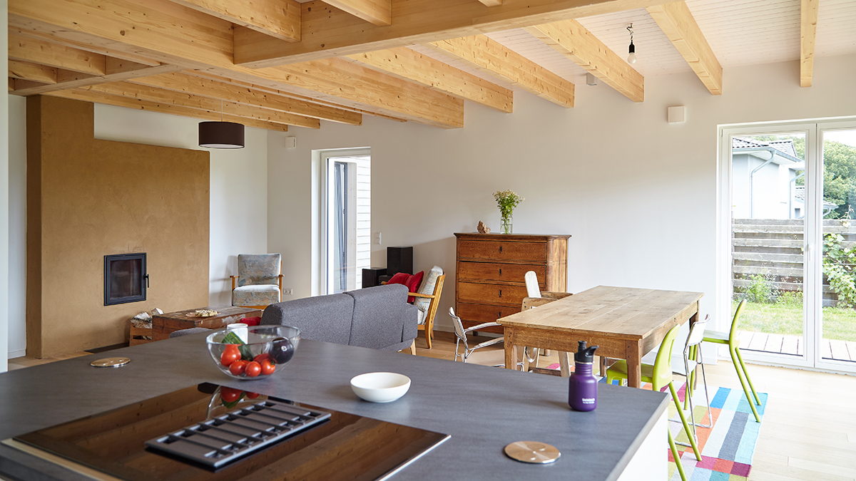 08_Modernes_Holzhaus_Offener_Grundriss_Offene_Holzbalkendecke_Grundofen_mit_Lehmputz