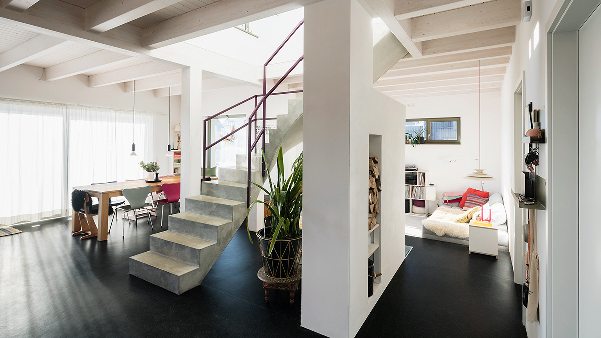 05_Modernes_Grundofenhaus_Offener_Grundriss_Ofen_unter_der_Treppe_Heller_Wohnraum_Weisse_Holzbalkendecke